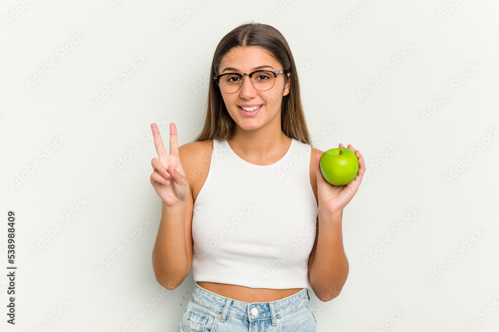 Young Indian woman holding an apple isolated on white background showing number two with fingers. Young Indian woman holding an apple isolated on white background showing number two with fingers.