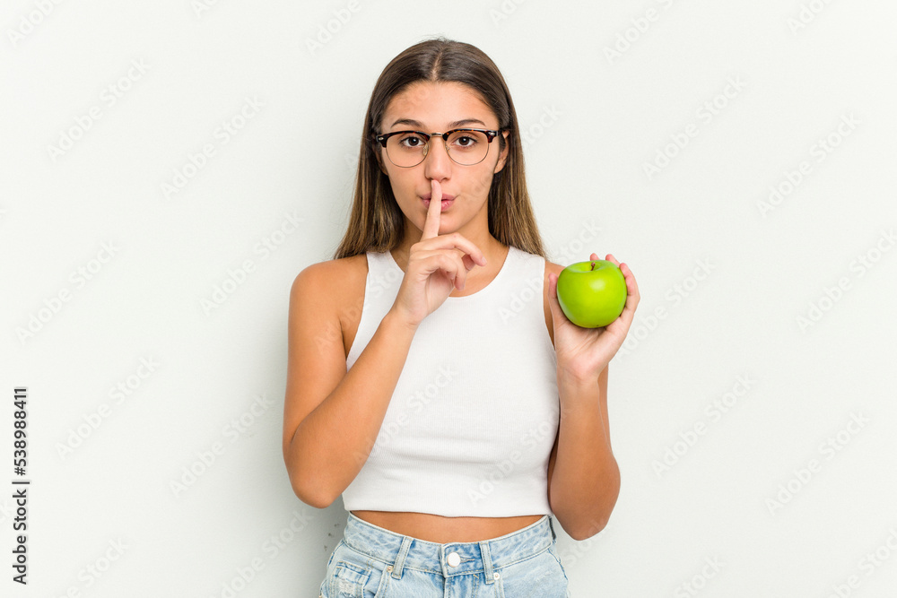 Young Indian woman holding an apple isolated on white background keeping a secret or asking for silence. Young Indian woman holding an apple isolated on white background keeping a secret or asking for silence.
