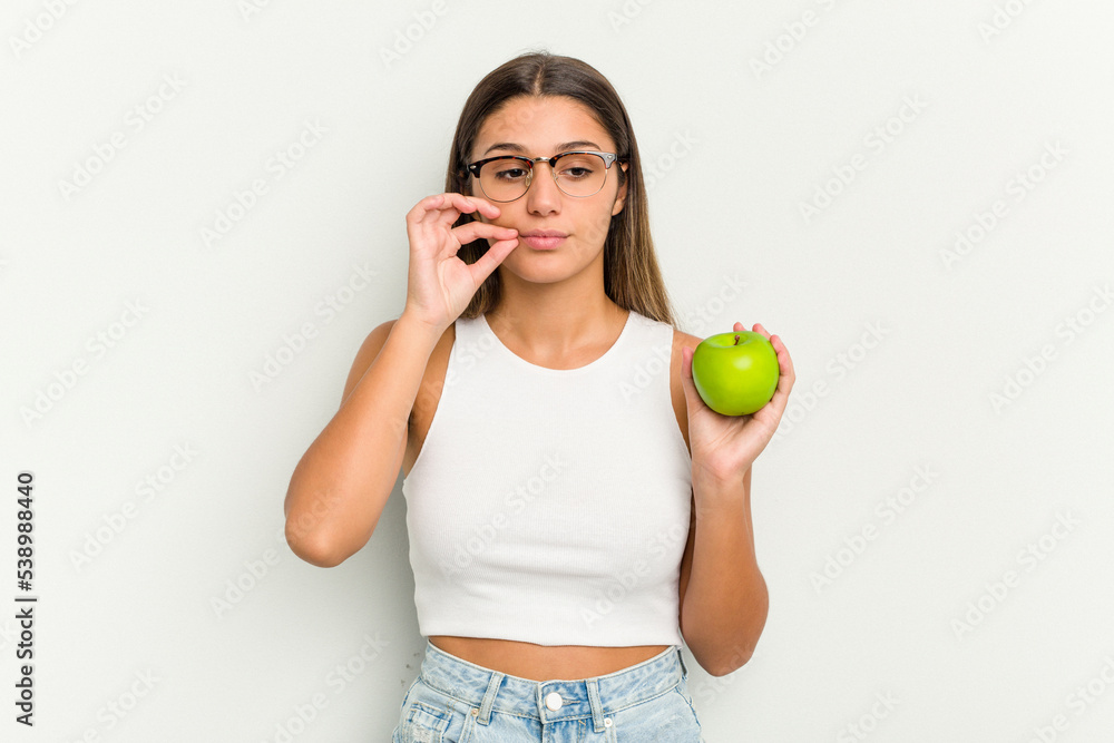 Young Indian woman holding an apple isolated on white background with fingers on lips keeping a secret. Young Indian woman holding an apple isolated on white background with fingers on lips keeping a secret.