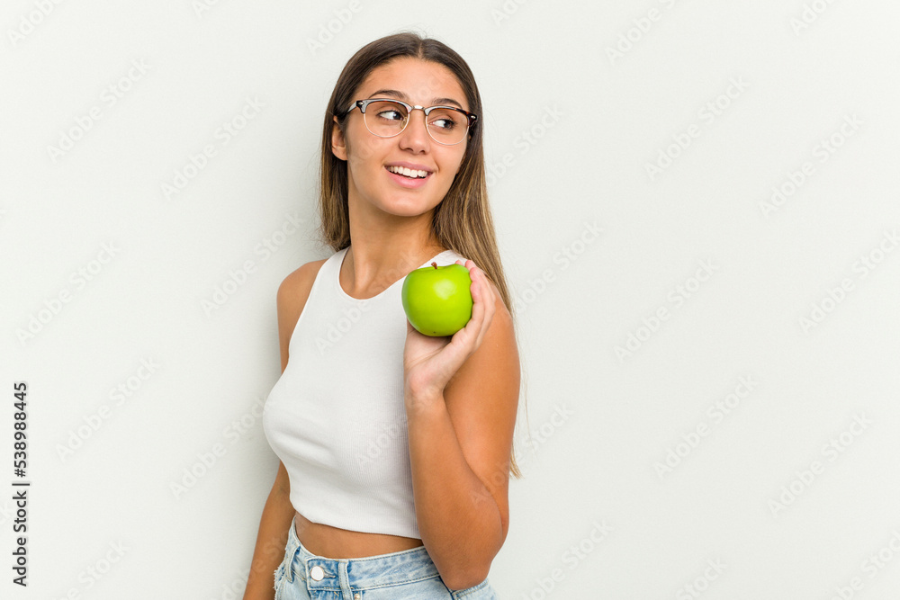 Young Indian woman holding an apple isolated on white background looks aside smiling, cheerful and pleasant. Young Indian woman holding an apple isolated on white background looks aside smiling, cheerful and pleasant.