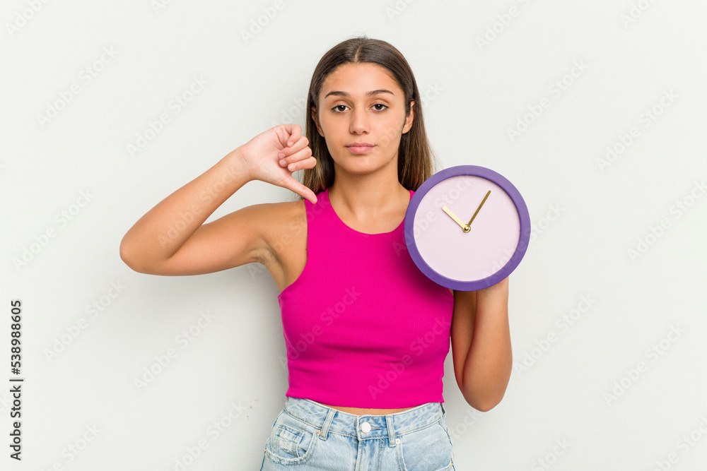 Young Indian woman holding a clock isolated on white background showing a dislike gesture, thumbs down. Disagreement concept. Young Indian woman holding a clock isolated on white background showing a dislike gesture, thumbs down. Disagreement concept.