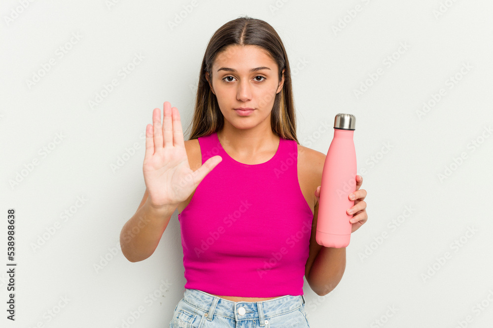 Young indian woman holding a pink thermo isolated on white background standing with outstretched hand showing stop sign, preventing you. Young indian woman holding a pink thermo isolated on white background standing with outstretched hand showing stop sign, preventing you.