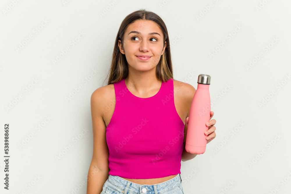 Young indian woman holding a pink thermo isolated on white background dreaming of achieving goals and purposes Young indian woman holding a pink thermo isolated on white background dreaming of achieving goals and purposes