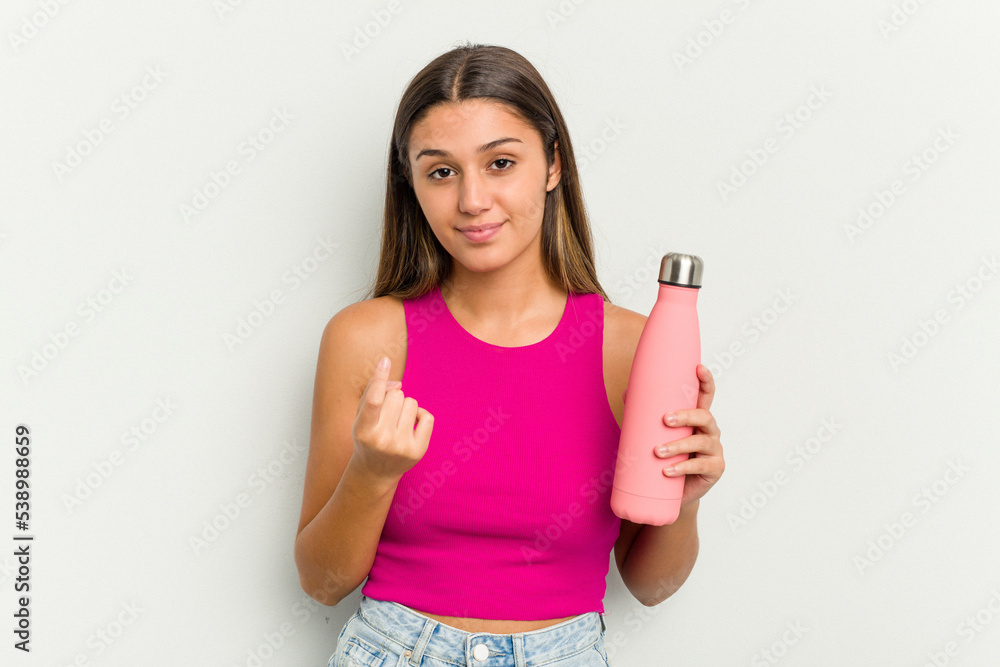 Young indian woman holding a pink thermo isolated on white background pointing with finger at you as if inviting come closer. Young indian woman holding a pink thermo isolated on white background pointing with finger at you as if inviting come closer.