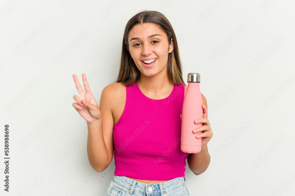 Young indian woman holding a pink thermo isolated on white background joyful and carefree showing a peace symbol with fingers. Young indian woman holding a pink thermo isolated on white background joyful and carefree showing a peace symbol with fingers.