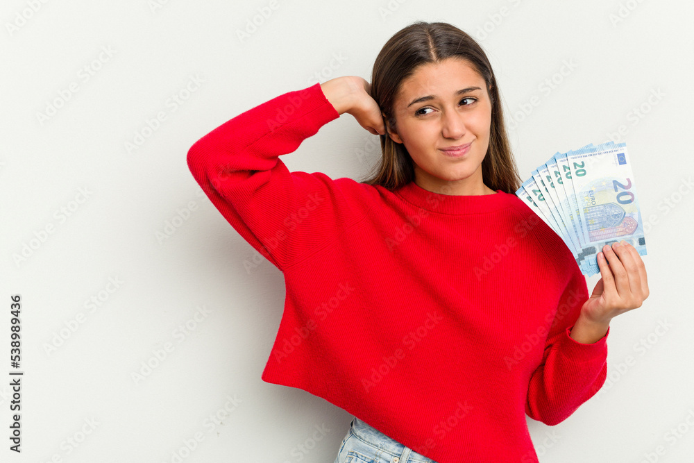 Young Indian woman holding a banknotes isolated on white background touching back of head, thinking and making a choice. Young Indian woman holding a banknotes isolated on white background touching back of head, thinking and making a choice.