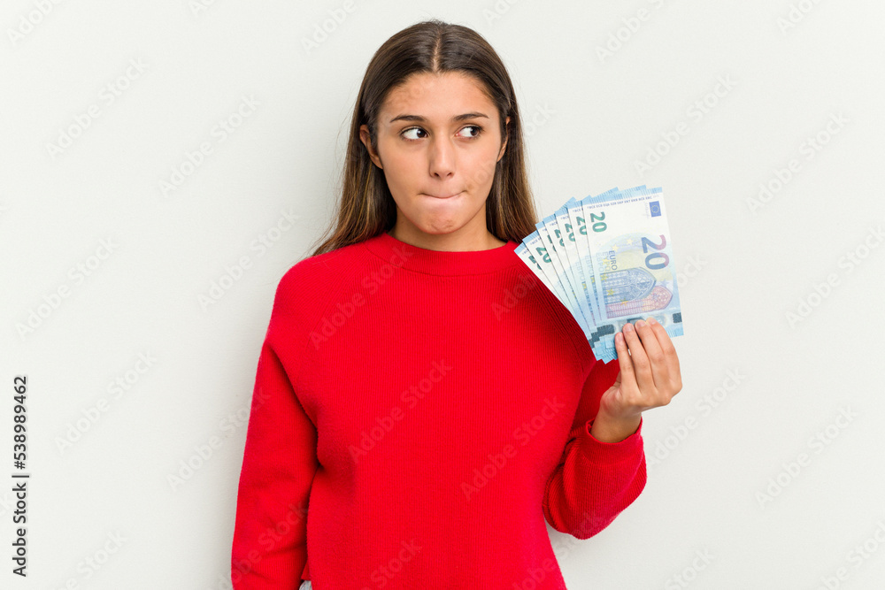 Young Indian woman holding a banknotes isolated on white background confused, feels doubtful and unsure. Young Indian woman holding a banknotes isolated on white background confused, feels doubtful and unsure.