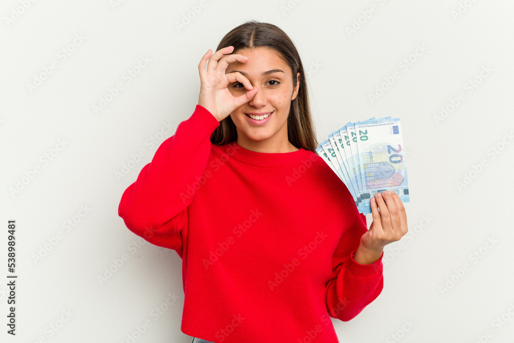 Young Indian woman holding a banknotes isolated on white background excited keeping ok gesture on eye. Young Indian woman holding a banknotes isolated on white background excited keeping ok gesture on eye.