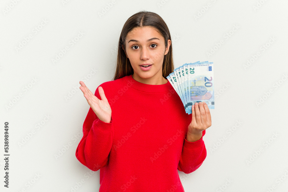 Young Indian woman holding a banknotes isolated on white background surprised and shocked. Young Indian woman holding a banknotes isolated on white background surprised and shocked.