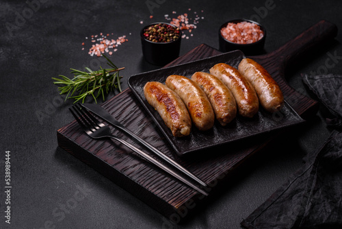 Tasty grilled sausages with spices and herbs on a black slate plate