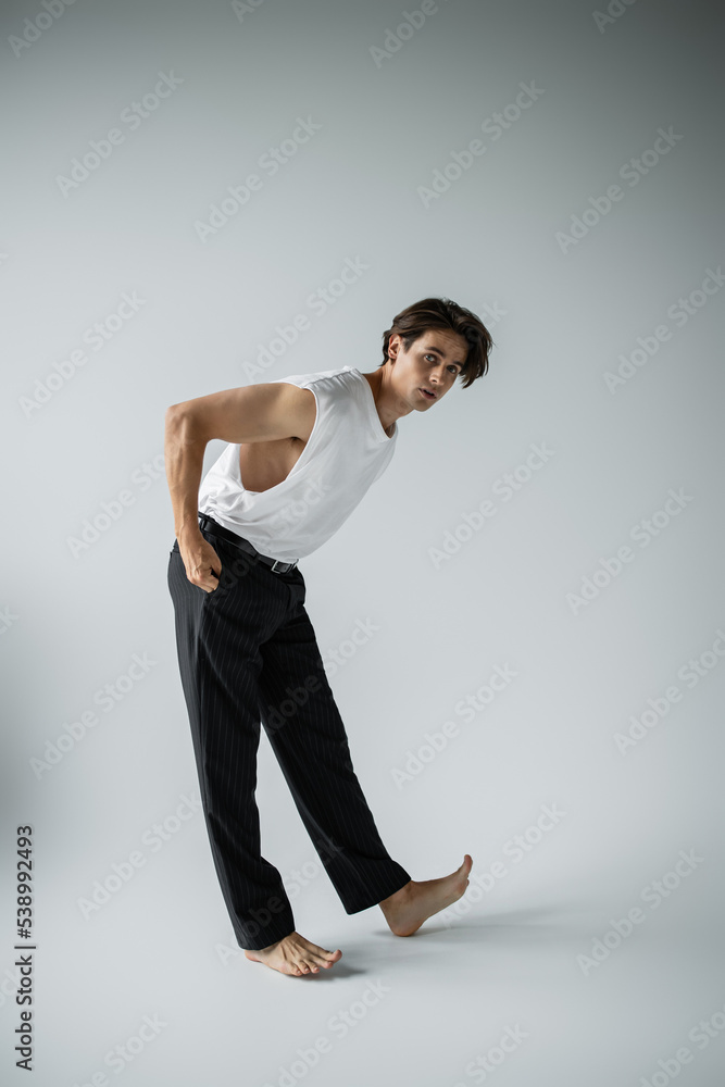 full length of stylish man in white t-shirt and black pants posing with hand in pocket on grey full length of stylish man in white t-shirt and black pants posing with hand in pocket on grey