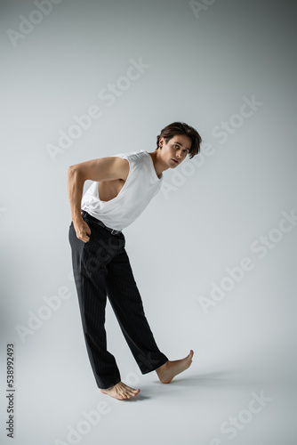 full length of stylish man in white t-shirt and black pants posing with hand in pocket on grey