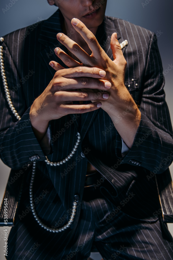 cropped view of stylish man in trendy suit with pearl chain gesturing on dark gray