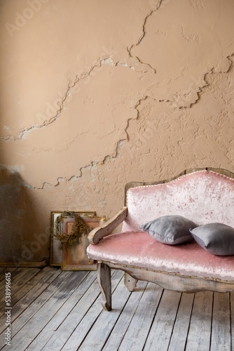 vintage baroque pink sofa stands on wooden floor, against textured wall
