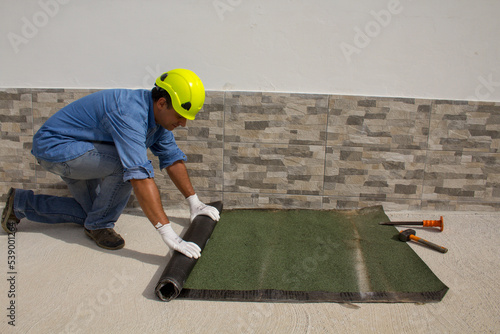 Construction worker at work while unrolling the tarred bituminous sheath to protect roofs and floors from bad weather and rain. Insulation in the construction sector. 