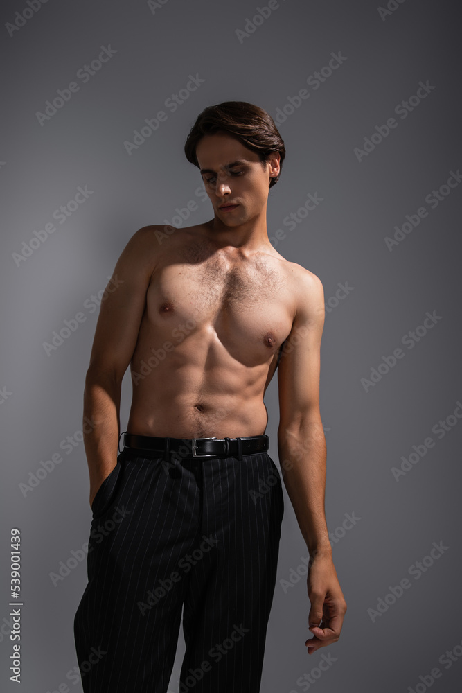 good looking man with muscular body posing with hand in pocket of black trousers on grey good looking man with muscular body posing with hand in pocket of black trousers on grey