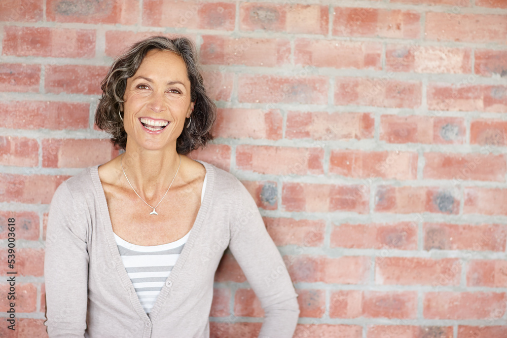 Laughing at her own jokes. A beautiful mature woman leaning against a wall outdoors. Laughing at her own jokes. A beautiful mature woman leaning against a wall outdoors.