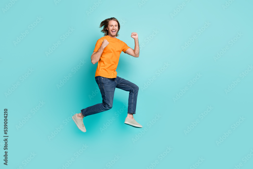 Full length photo of attractive lucky guy dressed orange t-shirt jumping high empty space isolated teal color background