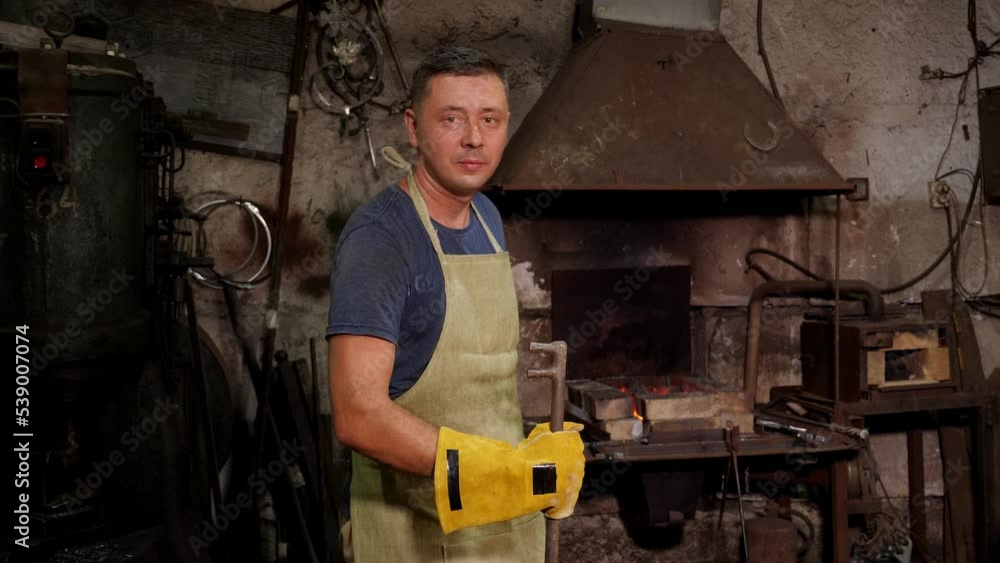 Portrait of a blacksmith in uniform with tools in an old forge, in the background a bonfire with burning hot coals. Portrait of a blacksmith in uniform with tools in an old forge, in the background a bonfire with burning hot coals.