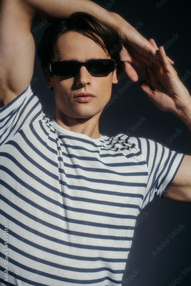 Stylish and muscular man in sunglasses posing isolated on grey with lighting Stylish and muscular man in sunglasses posing isolated on grey with lighting