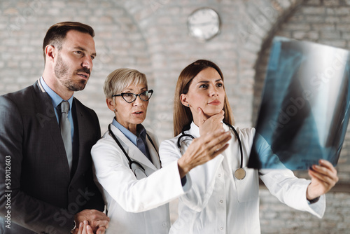 Two doctors and businessman examining X-ray image in the hospital