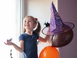 A cheerful funny girl puts a witch hat on a balloon, decorates the house for Halloween, fun, joy, happiness, smiles with her mouth wide open and looks up