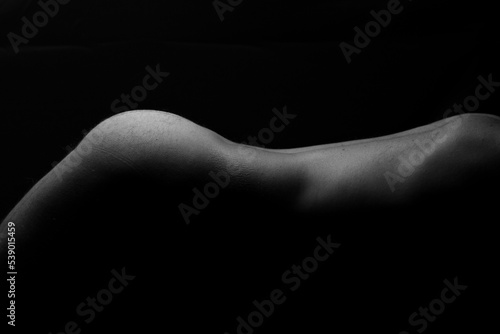Artistic nude with lighting on bare skin from the back to lower thighs of male model black background