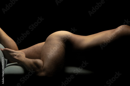young adult nude male fitness model in horizontal laying pose against black background