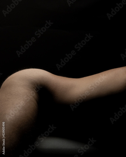 Young adult nude male fitness model lying pose against black background. naked man closeup on body fragment legs, back, and torso vertical