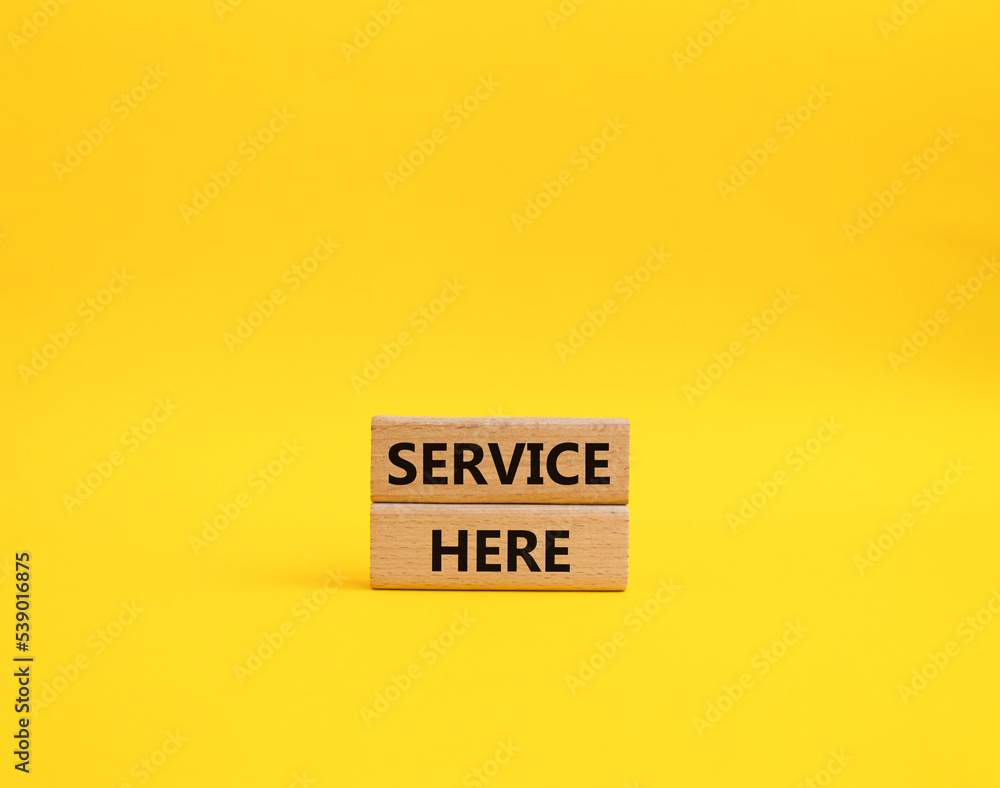 Service here symbol. Concept words Service here on wooden blocks. Beautiful yellow background. Business and Service here concept. Copy space. Service here symbol. Concept words Service here on wooden blocks. Beautiful yellow background. Business and Service here concept. Copy space.
