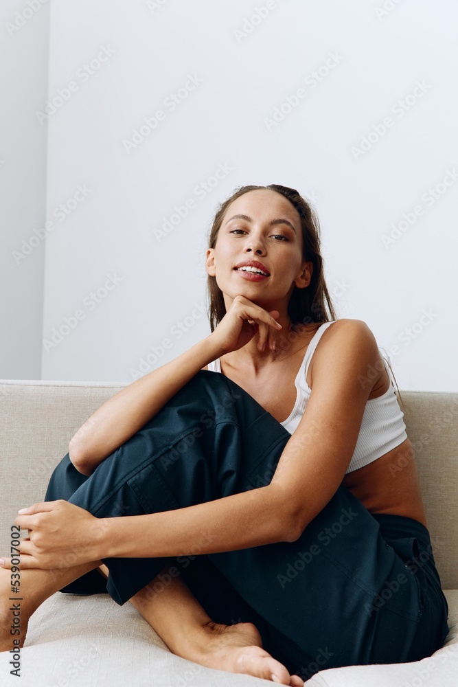 A woman sits relaxed on the couch and smiles looking at the camera in home clothes with long hair and tanned skin A woman sits relaxed on the couch and smiles looking at the camera in home clothes with long hair and tanned skin