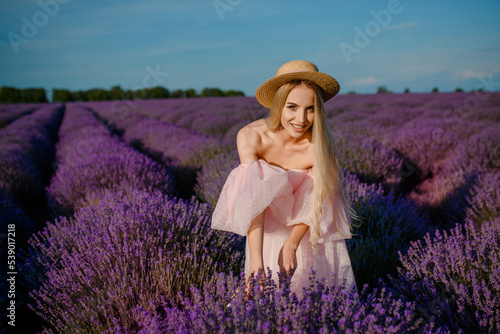 Portrait of a young beautiful happy smiling woman in a pink dress and a hat  walking in the lavender field
