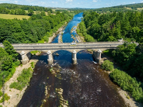 Aerial shot of the Bywell Bridge over the river Tyne in Northumberland with lush trees on both sides