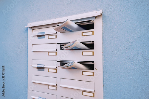 The mailbox of a residential building with daily newspapers sticking out with advertisements and news. photo