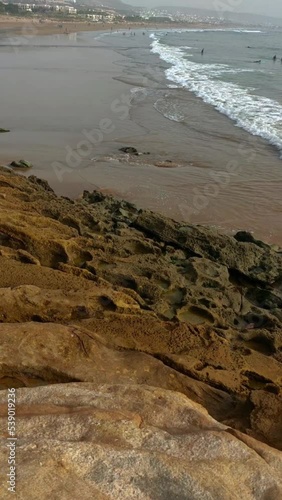 Man watching waves breaking on rocks with people doing surfing