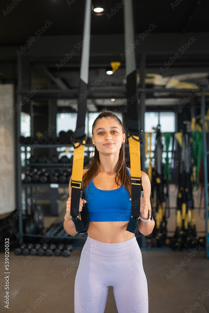 Woman doing exercises with trx fitness straps in the gym Woman doing exercises with trx fitness straps in the gym