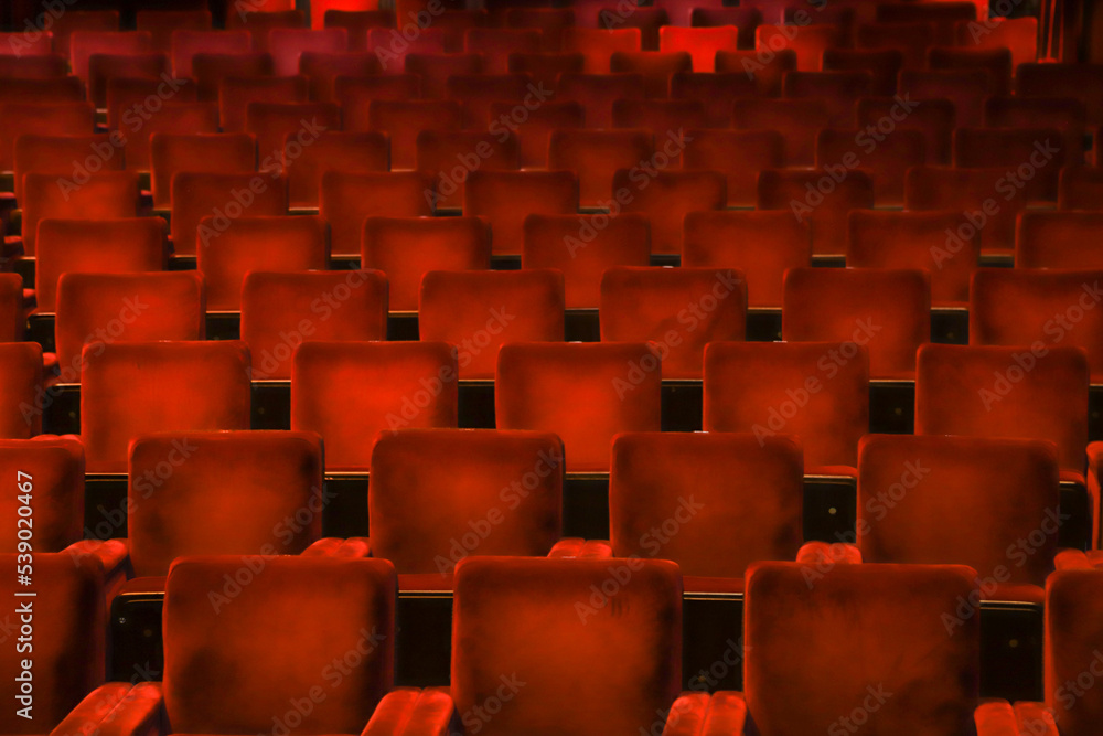 Obraz premium Red velvet chairs in a theater, highlighting the symmetry, lines and repetition of the seats. 