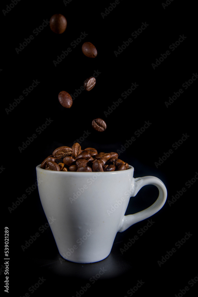 White cup with coffee beans on a black background White cup with coffee beans on a black background