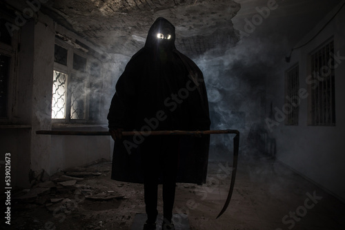 Fotografie death with scythe standing in the dark hall of abandoned building