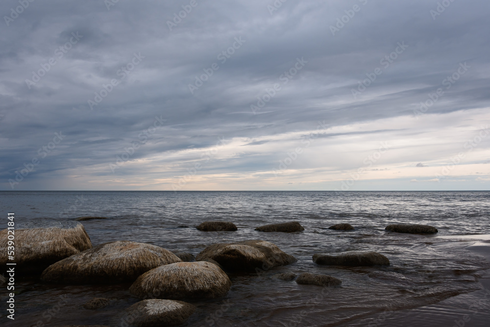 Baltic Sea before sunset. Evening cloudy sky over the coast of Narva Bay. The calm sea washes coastal granite stones. Northern seascape with light dramatic notes.