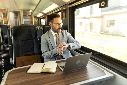 Young business man traveling to work by train.  Working while traveling, using laptop, mobile phone and notebook Thinking about new goals, noting, planning work © Nemanja