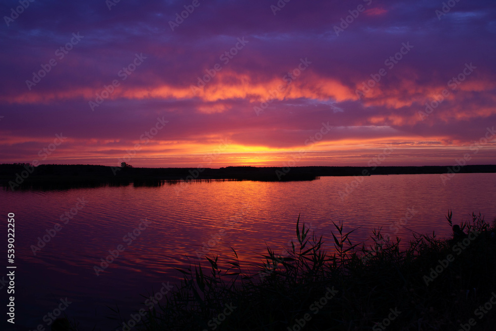 Beautiful sunset over the river. Magical sunrise behind colorful clouds over the lake. Calm water in a pond on the backdrop of a bright sky with a rising sun. Beauty natural wallpaper. Dawn nature