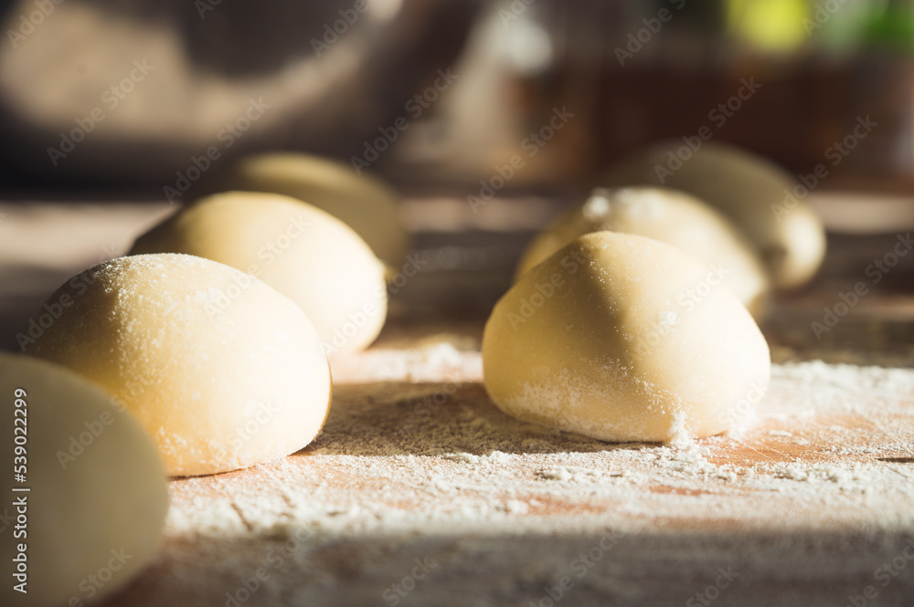 Close-up of raw dough balls and flour on wooden counter. Ready for baking. Sunlight. Close-up of raw dough balls and flour on wooden counter. Ready for baking. Sunlight.