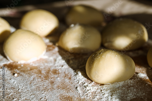 Close-up of raw dough balls and flour on wooden counter. Ready for baking. Sunlight.