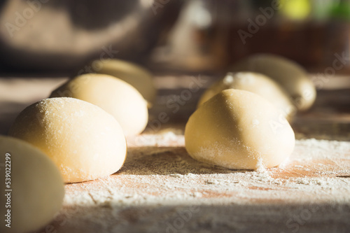 Close-up of raw dough balls and flour on wooden counter. Ready for baking. Sunlight.