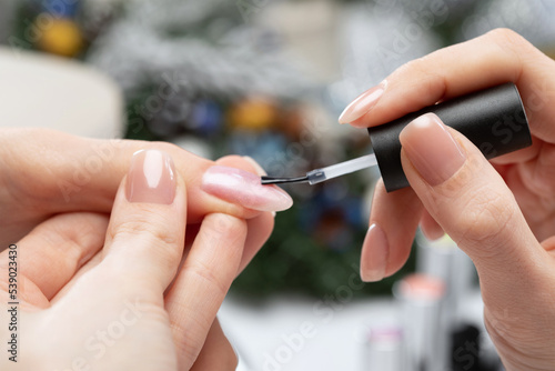 The master of the manicure coats nails with gel polish in the beauty salon. Professional care for hands. New Year concept.