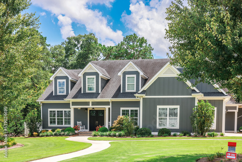 A large gray craftsman new construction house with a landscaped yard and leading pathway sidewalk