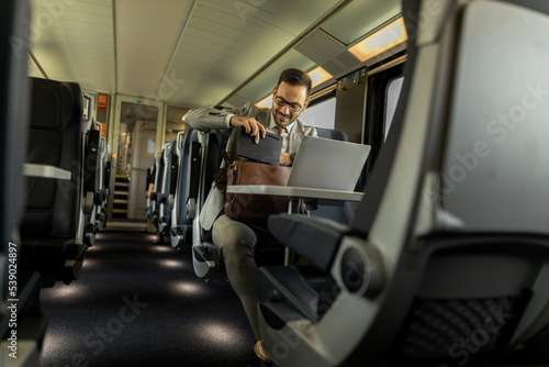 Formal wearing business man traveling to work by train. Business man is working while traveling, using laptop, mobile phone, and taking notes. Business man planning goals and meetings