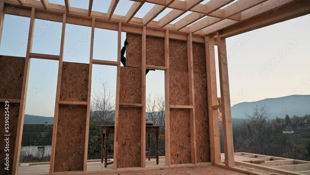 Carpenters mounting wooden OSB panel on the wall of future cottage. Men workers building wooden frame house. Carpentry and construction concept. Carpenters mounting wooden OSB panel on the wall of future cottage. Men workers building wooden frame house. Carpentry and construction concept.