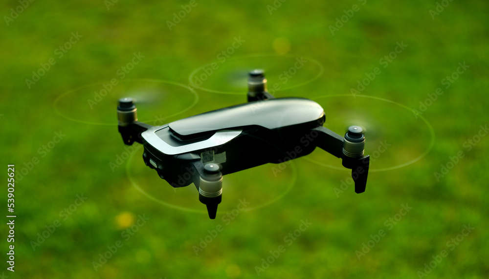 Flying spy drone with camera. A black copter flies over the green grass in the field. Shooting from the air. Flying spy drone with camera. A black copter flies over the green grass in the field. Shooting from the air.